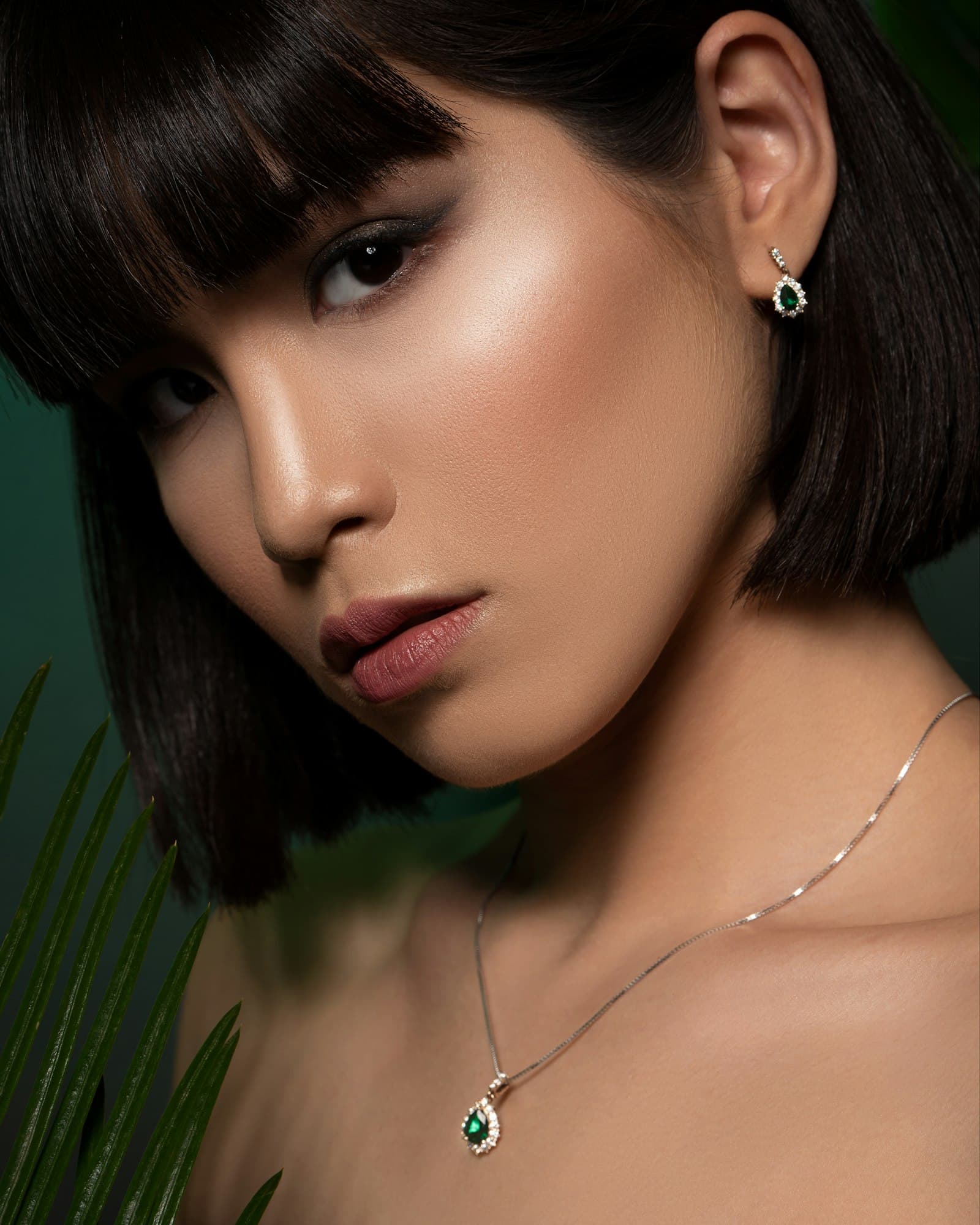 A woman wearing an emerald pendant and earrings against a deep green backdrop